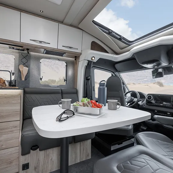 Moderner Camper-Innenraum mit Sitzgruppe und Tisch, Blick nach vorn ins Cockpit, Küche und Dachfenster.